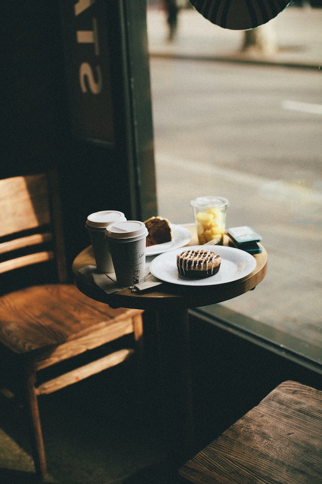 Una mesa de cafetería con dos tazas de café para llevar y una porción de torta.